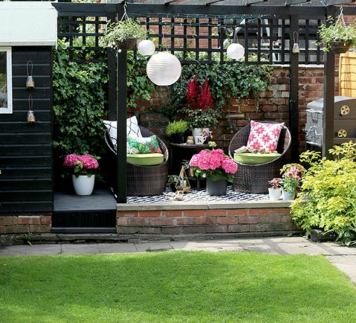 Zwart houten moderne pergola met twee rieten stoelen, witte Chinese lantaarns en potbloemen.