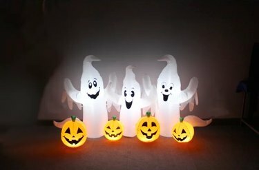 Tres fantasmas blancos con brazos sobre sus cabezas y cuatro calabazas como decoración inflable en un oscuro patio delantero.