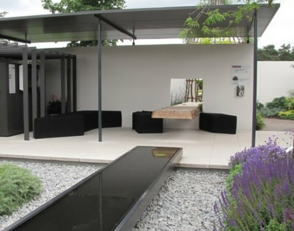 Overdekte moderne pergola met metalen dakbedekking, zwarte bank en stoelen, moderne fontein en inheemse planten.