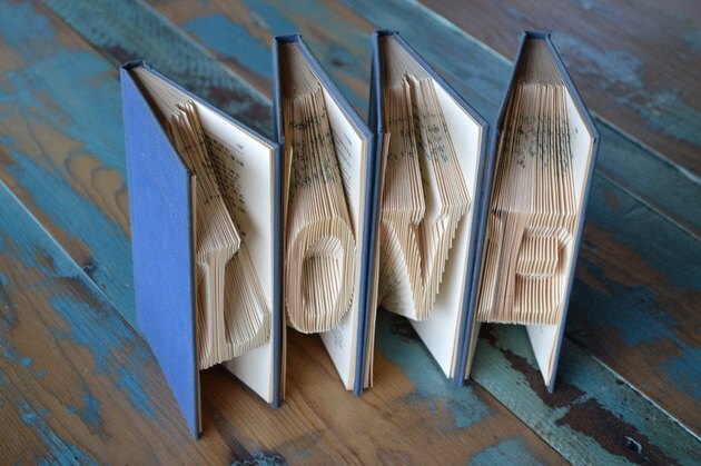 Escultura de quatro livros com capa azul e papel dobrado com a grafia "Amor"
