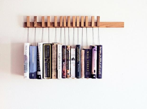 Estante de madeira montada na parede com livros pendurados em cordas