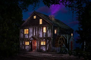 Esterno dell'Hocus Pocus Cottage di notte con finestre gialle incandescenti e fumo viola che esce dal camino.